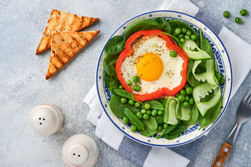 Red bell peppers stuffed with eggs, spinach leaves, green peas and microgreens on a breakfast plate on light grey table background. Top view.