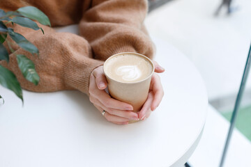 craft cup with cappuccino in the hands of a girl on the table close-up