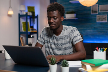 African american entrepreneur man browsing marketing information on laptop computer. Young freelancer working remote at online project in living room late at night. Virtual education