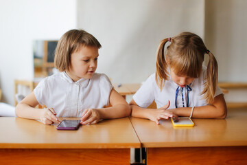 Girls friends schoolgirls desk with telephones, schoolchildren and gadgets, digital addiction at school,attention deficit disorder, clip thinking. Communication problems classmates with smart phones