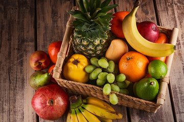 Mix of fresh juicy colorful exotic tropical fruits in basket on wooden background top view