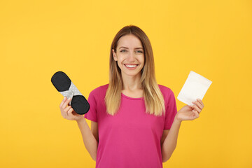 Happy young woman with disposable and reusable cloth menstrual pads on yellow background © New Africa