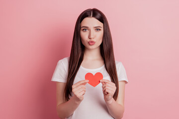 Portrait of attractive lovely cheerful girl send air kiss holding in hands small little heart isolated over pink background