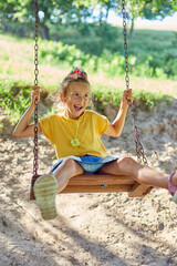 Similing little girl swinging on a large rustic wooden swing in the park, sunlight