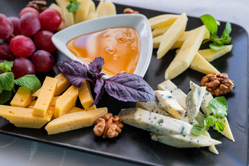 assorted food parmesan cheese with grapes and blue cheese and honey on a plate in a restaurant
