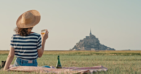 Young woman wearing hat picknick drink wine in front of mont saint michel 