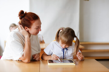 teacher and girl student child at school at desk works with digital tablet, gadgets in classroom...