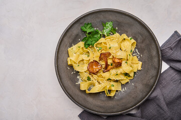 Traditional Italian pasta pappardelle with mushrooms chanterelles, cheese and parsley on dark plate and napkin, top view