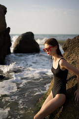 woman in swimsuit sunglasses ocean rocks posing