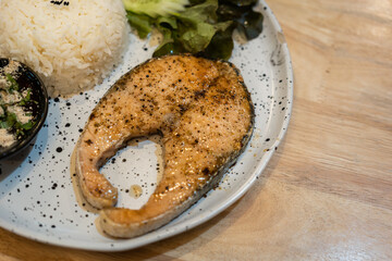 A big piece of grilled salmon steak with rice in white plate is served on wooden table. Food in plate object photo. Close-up.