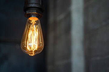 Close-up at classic style lighting bulb which is glowing in warm light shade, with blurred background of brick wall. Interior decoration and electric equipment object photo.