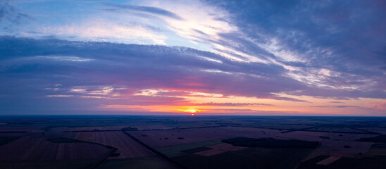 Wide panorama of setting sun over agricultural fields. Bright photo of clouds during the sunset - Powered by Adobe