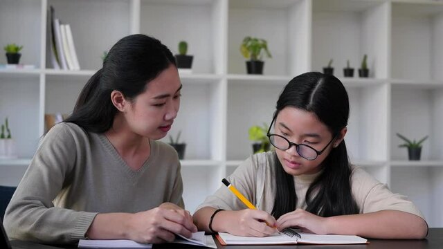 Concentrated asian girl is learning with private tutor at home.
