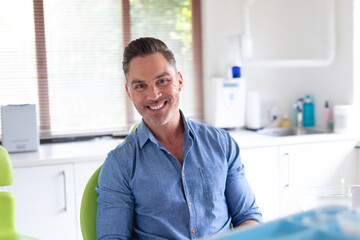 Portrait of smiling caucasian male patient looking at camera at modern dental clinic