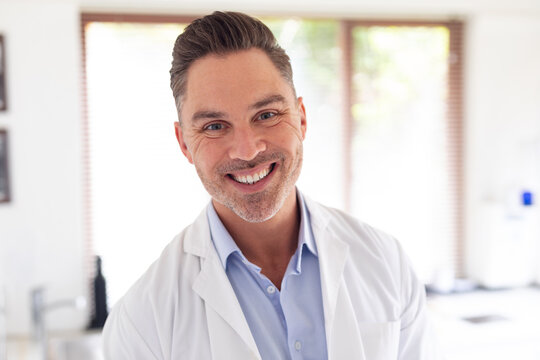Portrait of smiling caucasian male dentist looking at camera at modern dental clinic