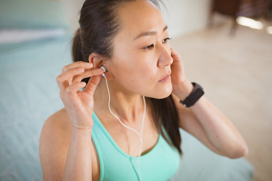 Portrait of asian woman in fitness clothes, preparing for exercise, putting on earphones