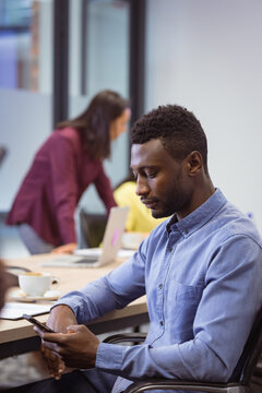 African american disabled businessman using smartphone and sitting in wheelchair in modern office