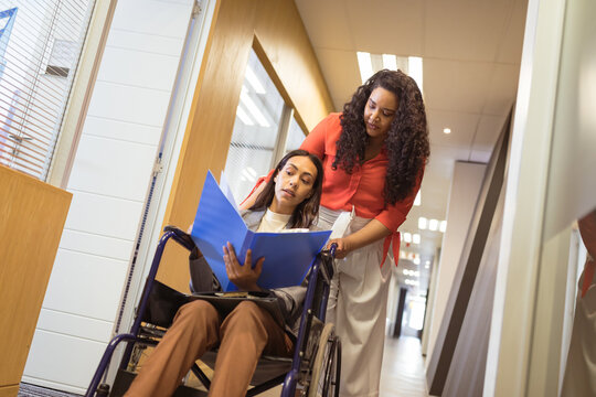 Biracial businesswoman in wheelchair talking with biracial businesswoman in modern office