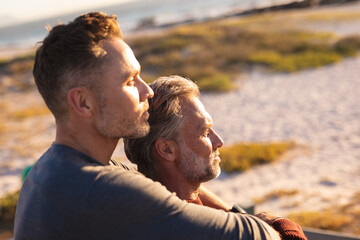 Happy caucasian gay male couple embracing in sun at seaside