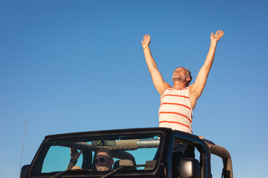 Happy caucasian gay male couple raising arms sitting in car on sunny day at seaside - Powered by Adobe