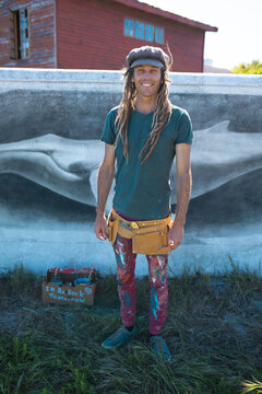 Smiling portrait of male hipster artist with messy clothing standing against whale mural painting