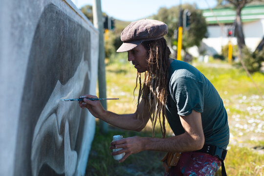 Male artist concentrating while making creative whale mural painting on wall with paintbrush
