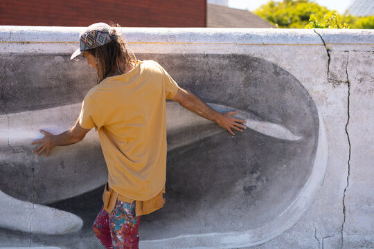 Rear view of male artist walking while touching whale mural painting on wall