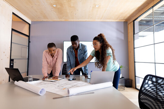 Multiracial male and female architects in casuals discussing over blueprint at conference table