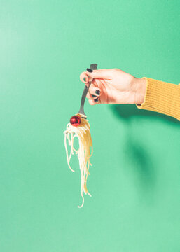 Creative composition with woman hand holding fork with spaghetti and red Christmas decoration against green background.