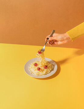 Creative retro scene with spaghetti plate and woman hand holding fork and red Christmas bauble against duo tone yellow and brown background. Vintage christmas dinner concept.