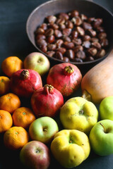 Pan with chestnuts, butternut squash and various fruit on dark background. Selective focus.