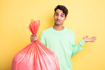 young handsome man feeling puzzled and confused and doubting. trash bag concept