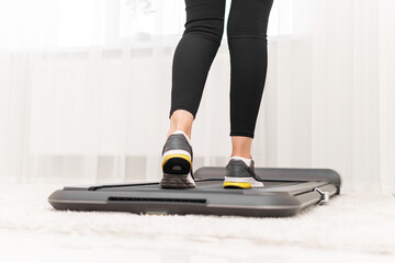 Sporty woman using walking treadmill in the interior of the room or home.