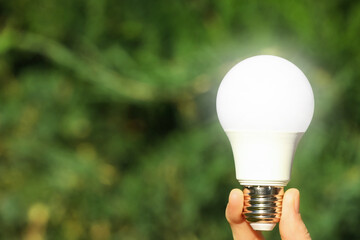 Woman holding glowing light bulb outdoors, closeup. Space for text