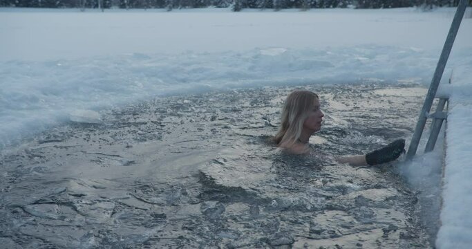 Winter ice hole swimming woman dipping in ice cold water in frozen lake