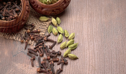 Colorful spices cloves, cardamom and black pepper on wooden background with copy space.