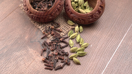 Colorful spices cloves, cardamom and black pepper on wooden background with copy space.