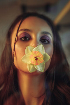 Young woman behind a glass wall with a flower in her mouth. Creative portrait.