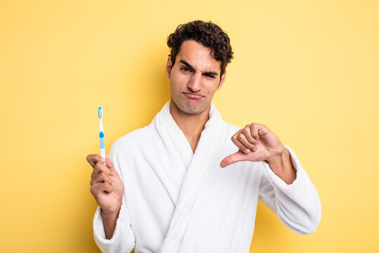 young handsome man feeling cross,showing thumbs down. bathrobe and toothbrush concept - Powered by Adobe