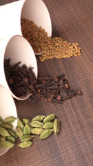 Colorful spices cloves, cardamom and black pepper on wooden background with copy space.