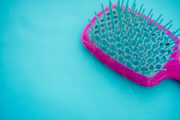 a lot of loose blond hair in a bright pink comb on a blue background. hair loss after illness. consequences of covid-19. fight against female alopecia.