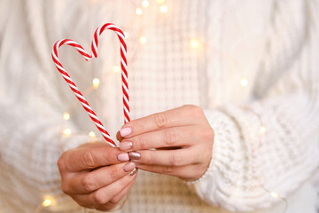 Close-up of women's hands holding candy canes in the form of heart.