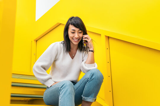 Happy young ethnic woman having phone conversation sitting on stairs