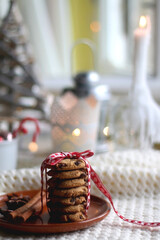 Stack of chocolate chip cookies tied with ribbon, cinnamon, anise, various Christmas decorations and lit candles. Hygge at home. Selective focus.