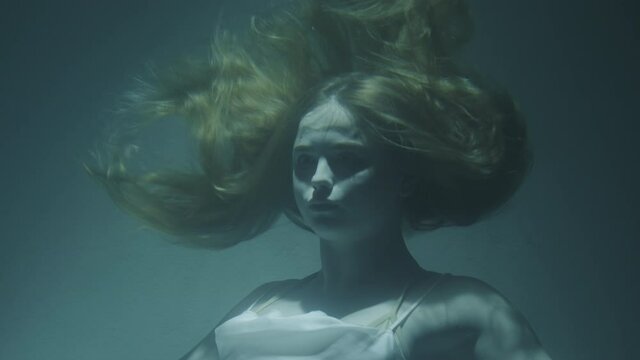 Close-up of a beautiful girl with red hair in a white dress froze under water