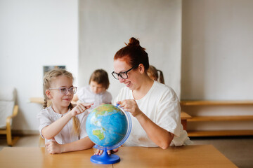 a teacher and a girl, a student, a child at school at a desk working with a globe, a teacher and a student are studying geography, looking for countries on the map. , modern education and technology
