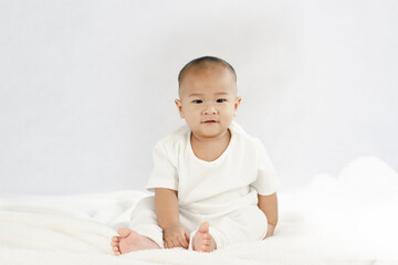 Charming 9 month old baby in white clothes on the bed
