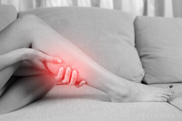 A woman suffering from feeling knee pain sitting sofa at home. hand massaging her painful knee....