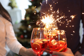 Three glasses with cocktails and sparklers on background of New Year tree