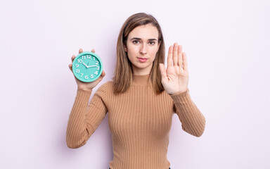 young pretty woman looking serious showing open palm making stop gesture. alarm clock